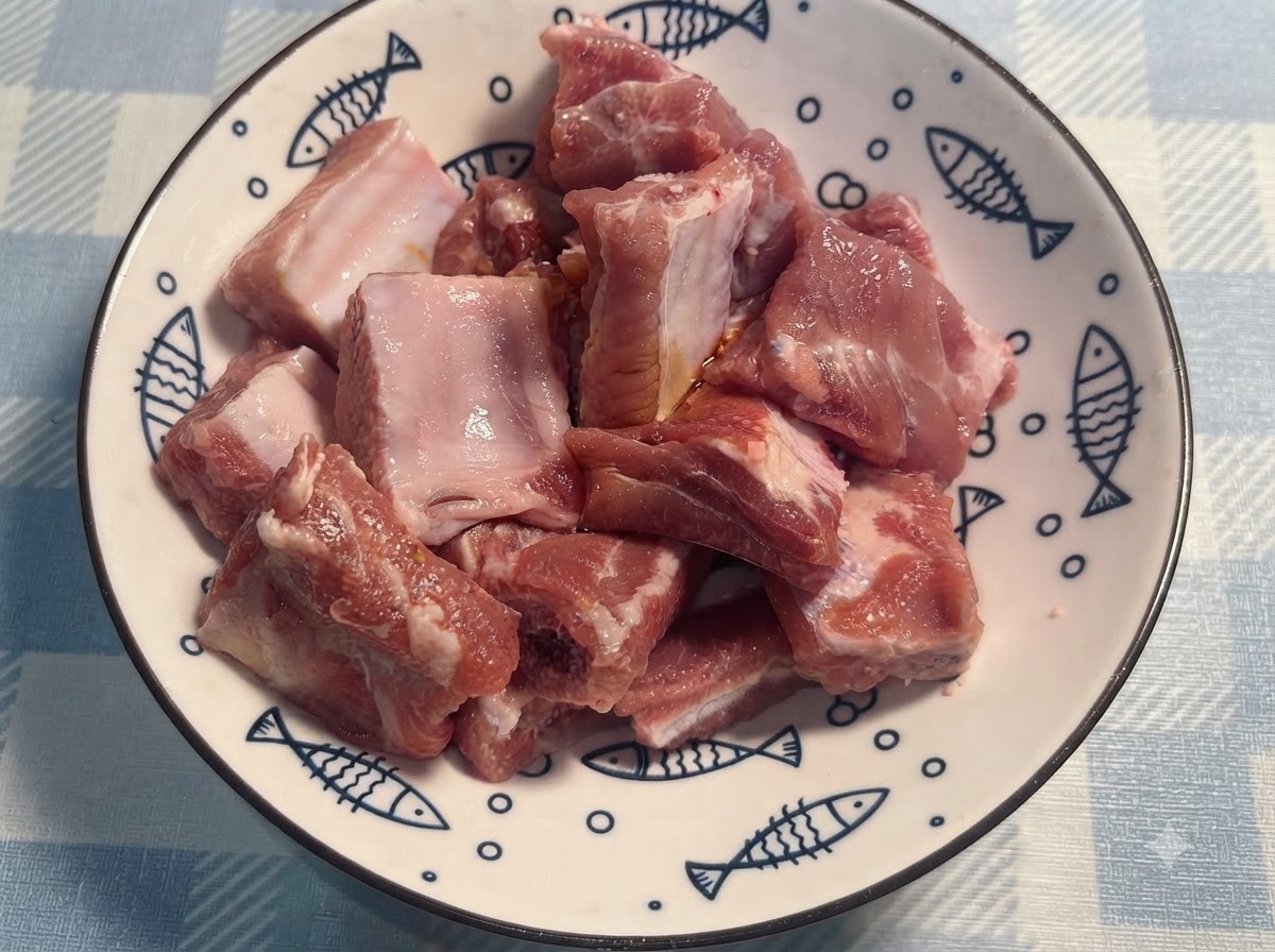 Mani con i guanti che mescolano e rigirano le costine di maiale condite in un piatto bianco.