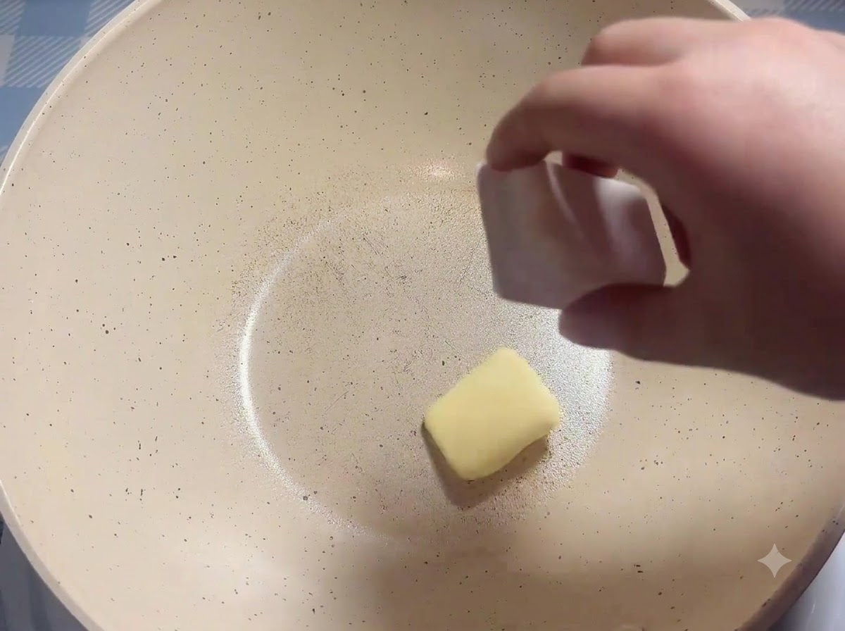 Un panetto di burro inserito in una padella bianca riscaldata.