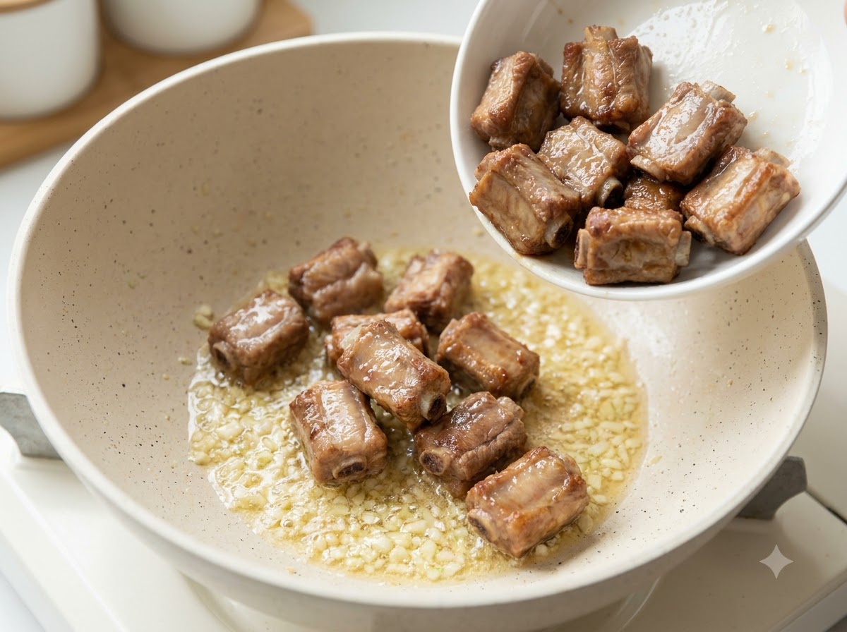 Costine di maiale fritte versate in una padella contenente aglio tritato e burro soffritti.