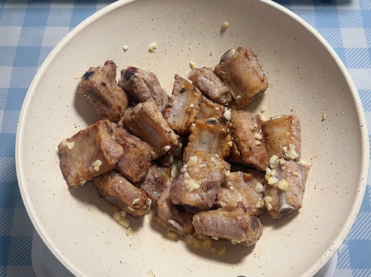 Costine di maiale condite con la salsa allinterno di una padella bianca.