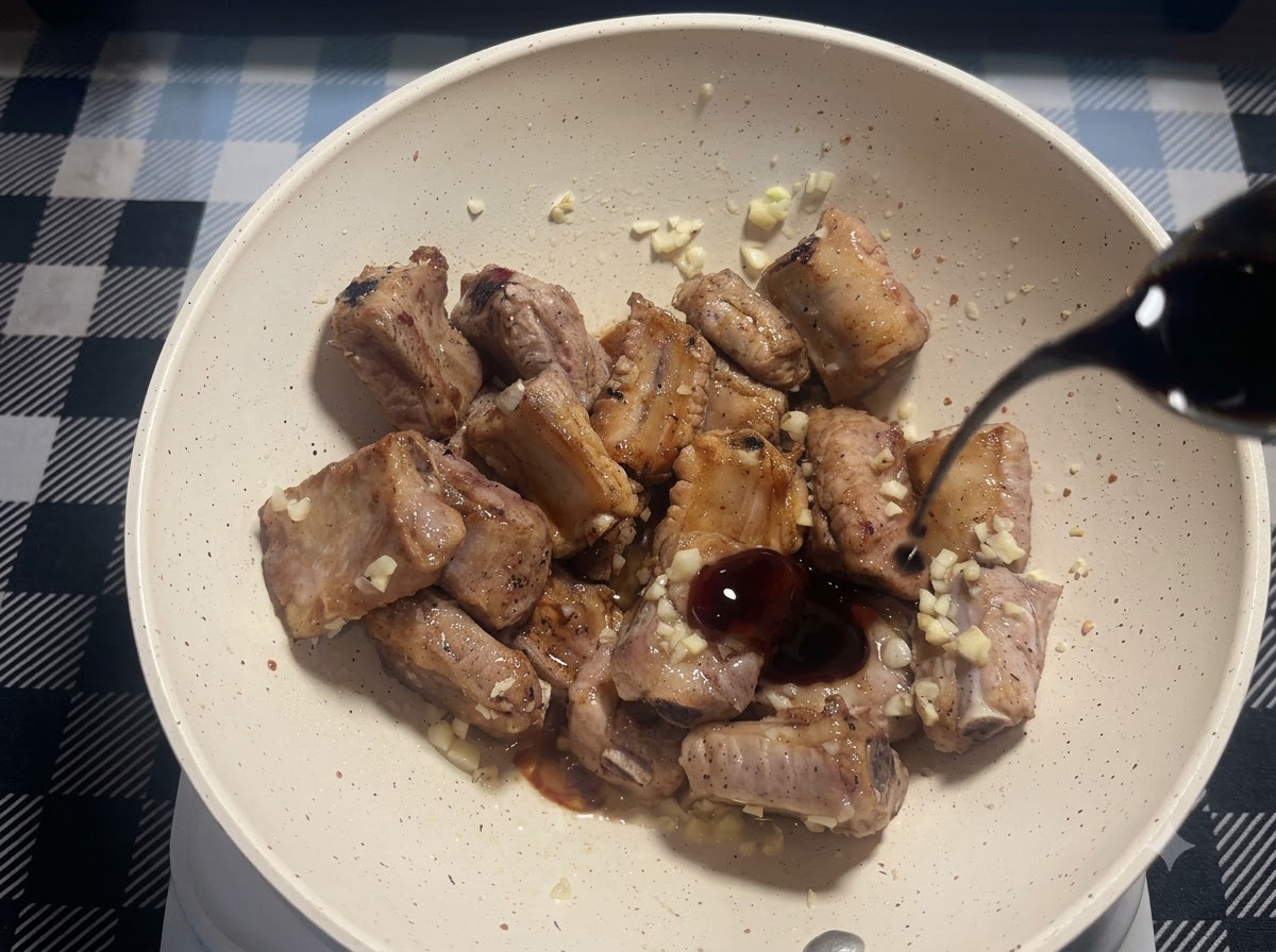 Un piccolo filo di salsa di soia scura versato nella padella con le costine di maiale fritte e laglio tritato.