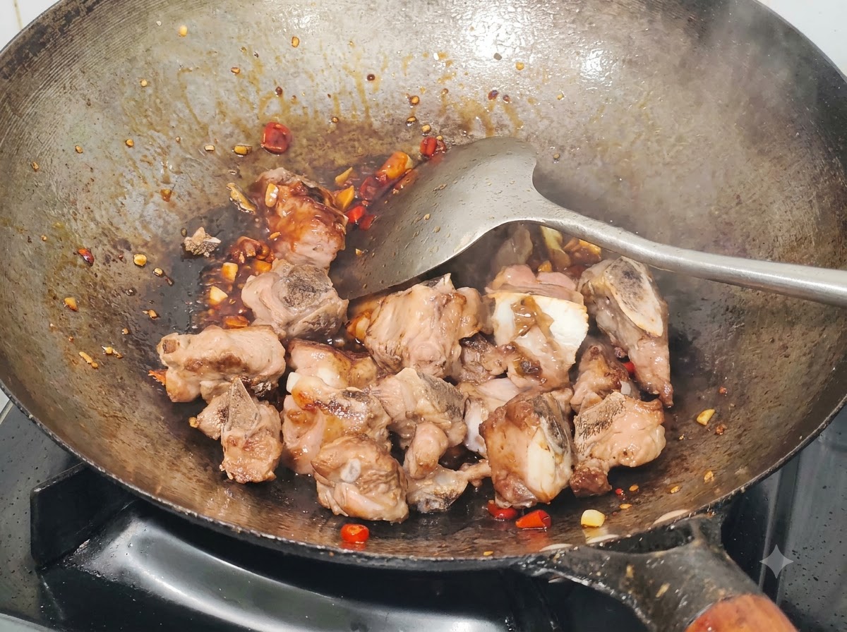 Costine di maiale fritte mescolate in un wok con salsa, peperoncini di miglio tritati e aglio usando una spatola di metallo.
