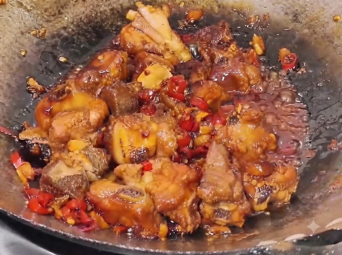Costine di maiale che sobbollono in una salsa densa e scura con pezzi visibili di peperoncino rosso e pezzetti daglio in un wok.
