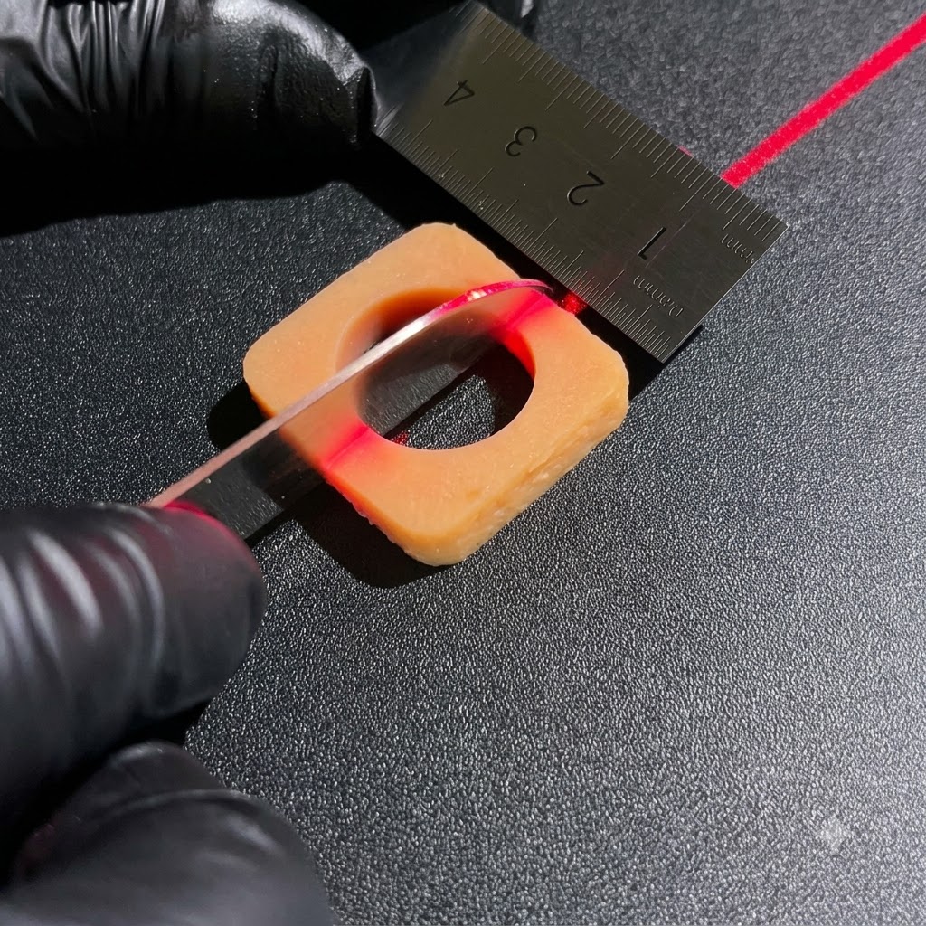 Mani con guanti che usano un coltello affilato e un righello di metallo per tagliare con precisione blocchi di ingredienti quadrati sotto una linea di allineamento laser rossa.
