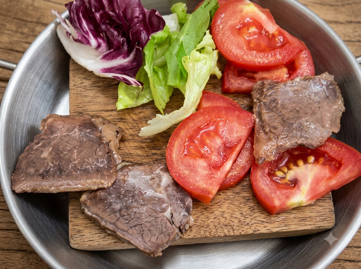 Lattuga fresca, pomodori a fette e pezzi di carne cotta disposti su un piccolo tagliere di legno.