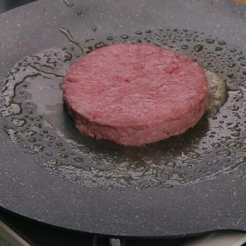 Un patty di manzo crudo in cottura nel burro allinterno di una padella calda.