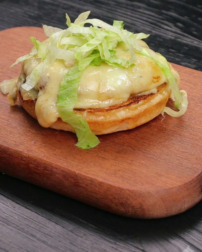 Lattuga fresca tagliata accumulata ordinatamente sopra un formaggio fuso e un patty di manzo poggiato su una base di panino tostato.