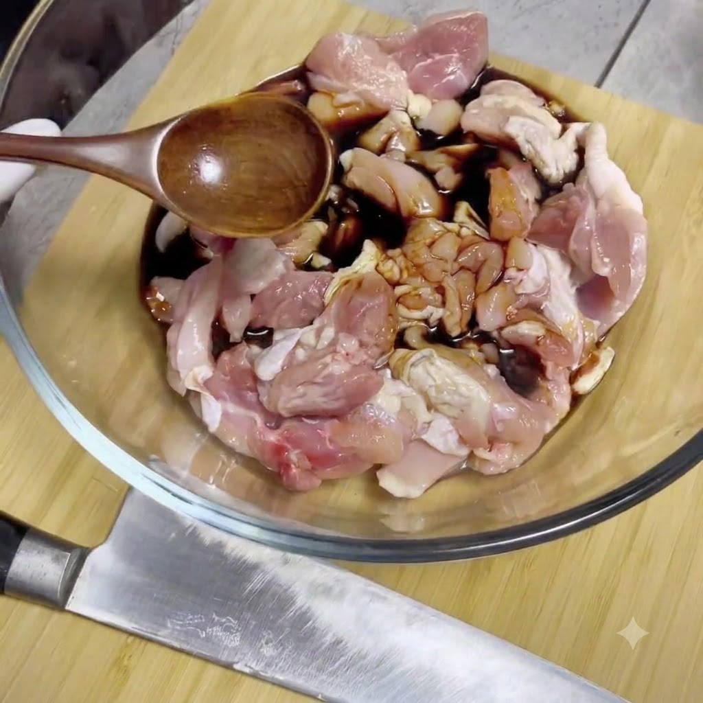 Salsa di soia versata da un cucchiaio di legno sui pezzi di pollo crudo allinterno di una ciotola di vetro.