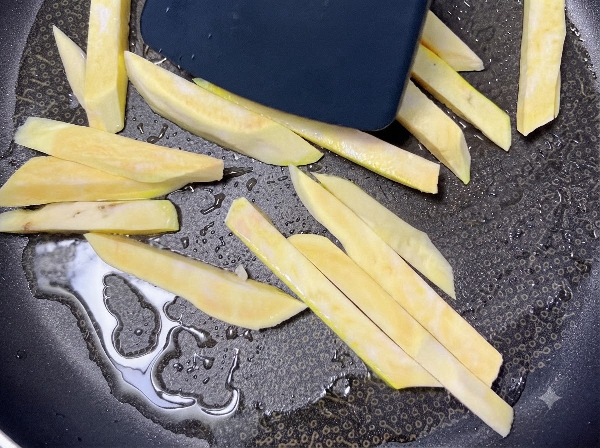 Bastoncini di patata dolce cruda che sfrigolano in una padella nera riscaldata con olio mentre vengono mossi con una spatola.