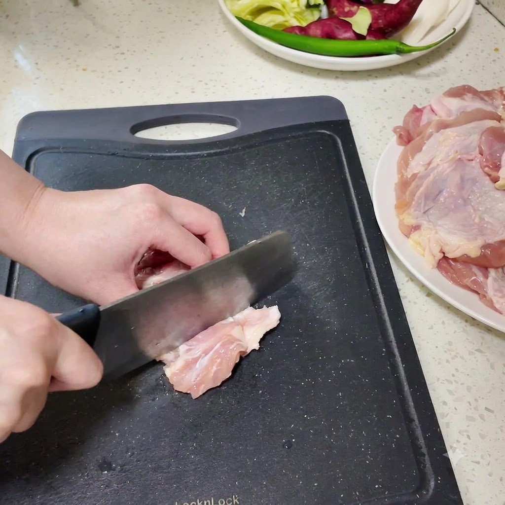 Fusi di pollo disossati tagliati a pezzi più piccoli su un tagliere nero.