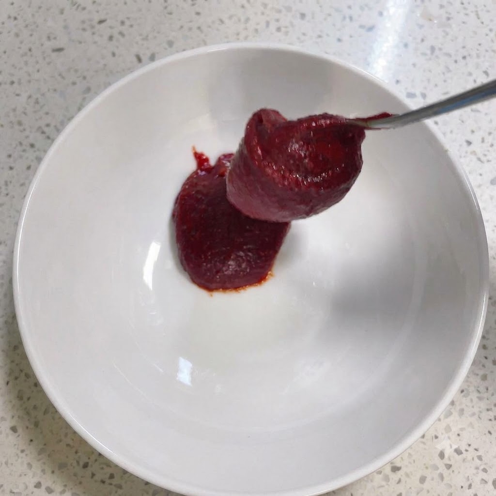 Pasta di peperoncino coreana e altri condimenti mescolati allinterno di una ciotola bianca.