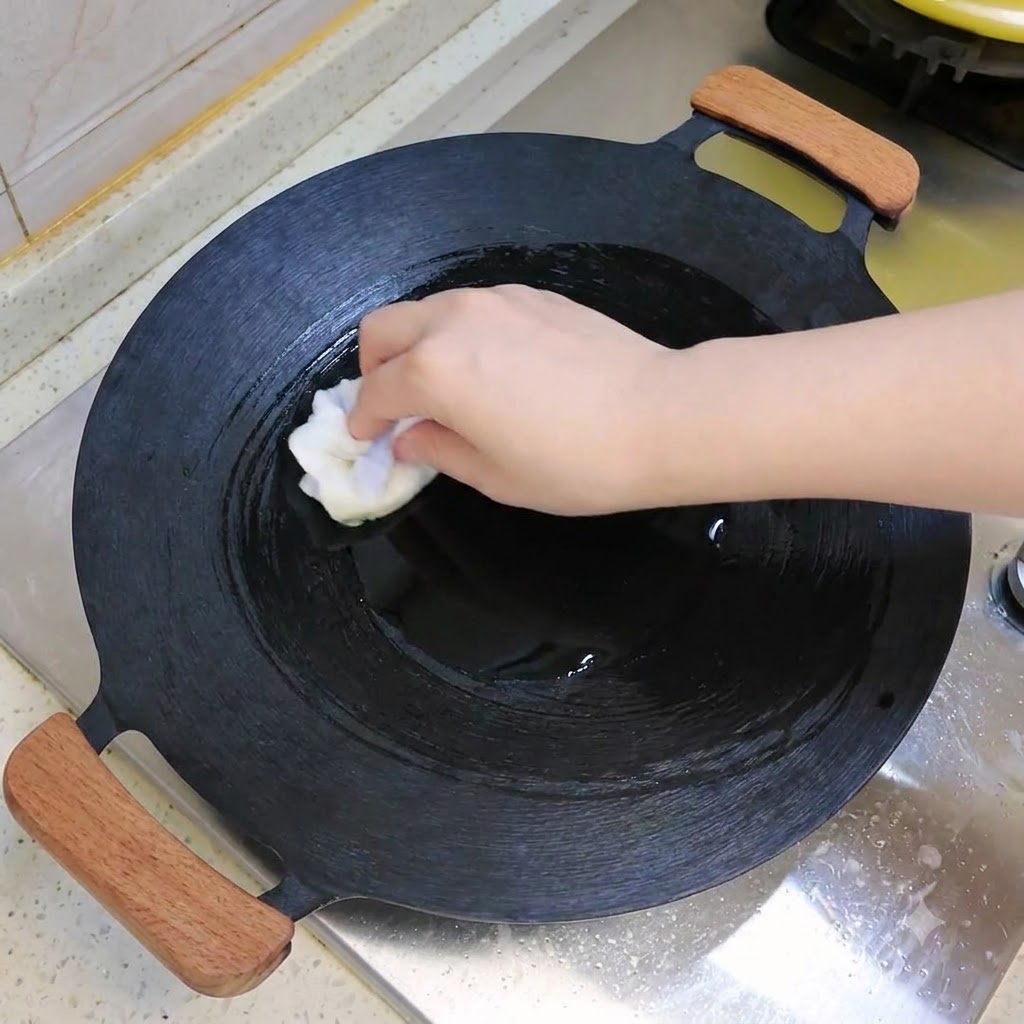 Un wok scuro pulito o oleato con un panno bianco su un piano cottura.