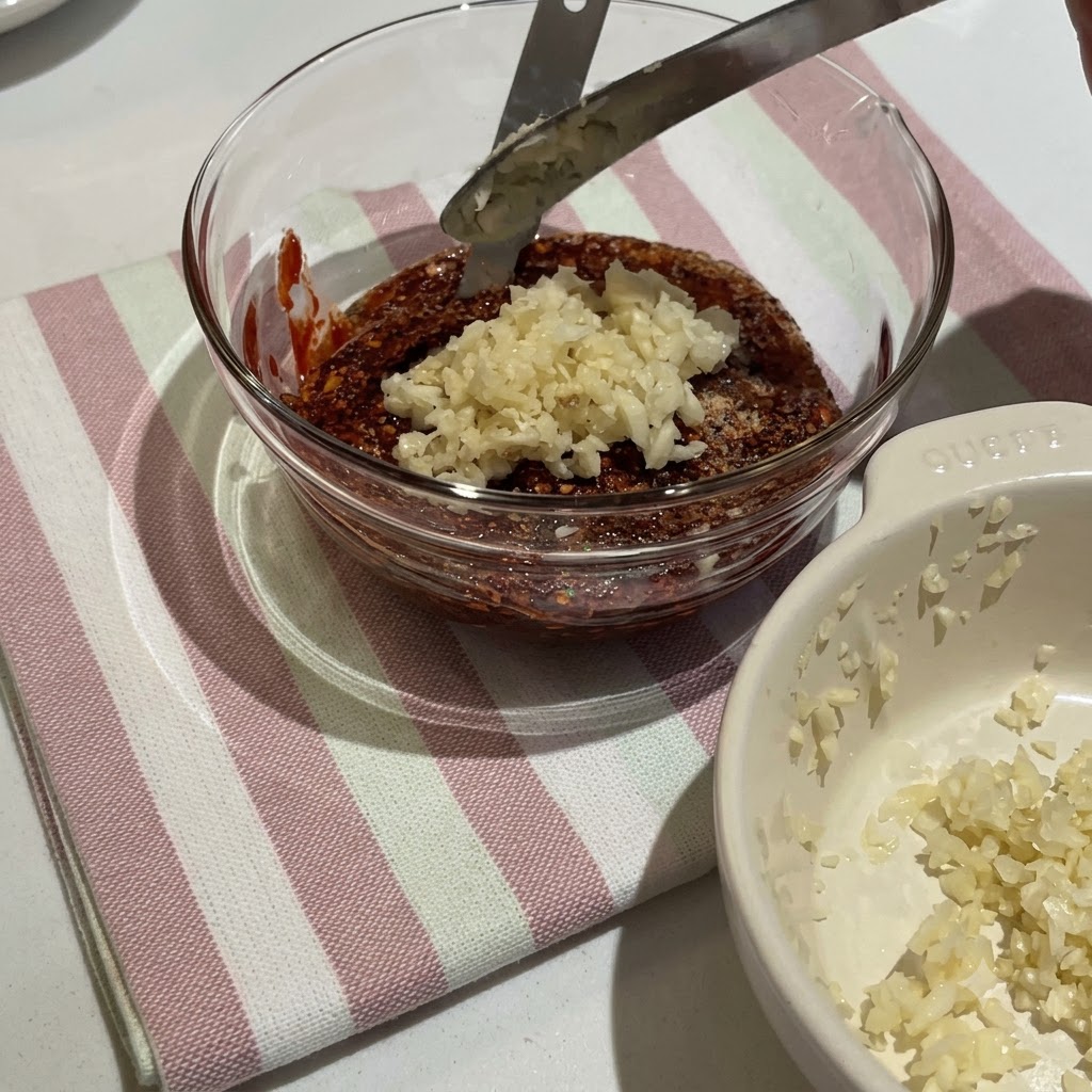 Pasta di peperoncino coreana e vari condimenti mescolati in una ciotola di vetro per creare una densa salsa rossa.
