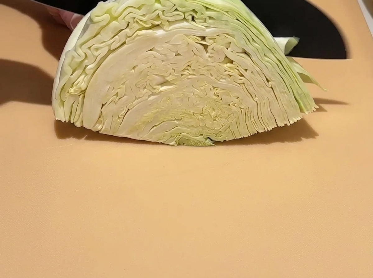 Uno spicchio di cavolo verde crudo tagliato a pezzi più piccoli su un tagliere con un coltello.