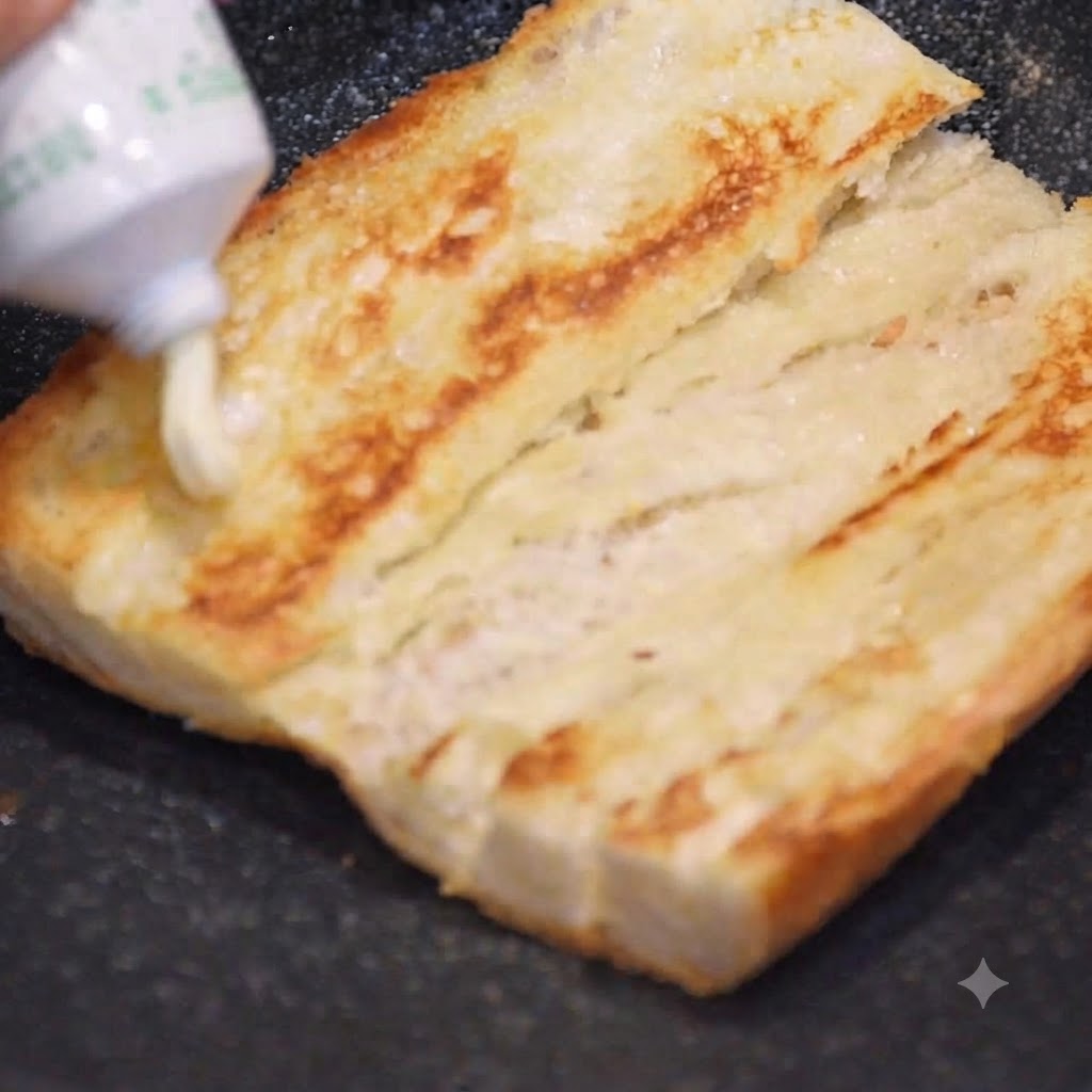 Maionese spremuta da un tubetto su una metà di baguette dorata e tostata.