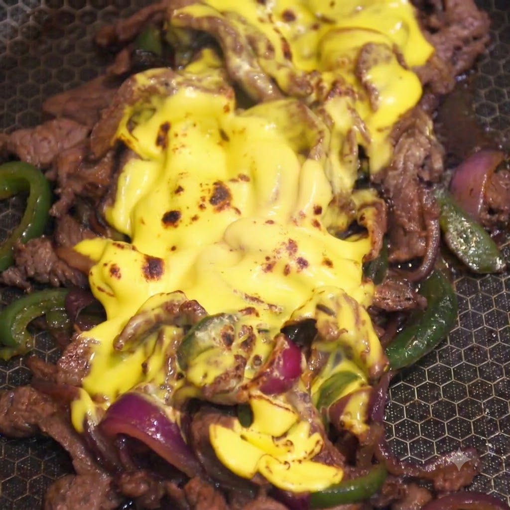Un cannello da cucina che fiammeggia lo strato di formaggio giallo fuso sul composto di manzo e verdure in una padella.