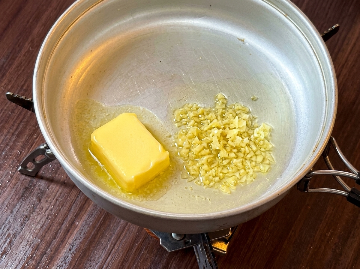 Una fetta di burro giallo che si scioglie in una padella di metallo su un fornello da campeggio.