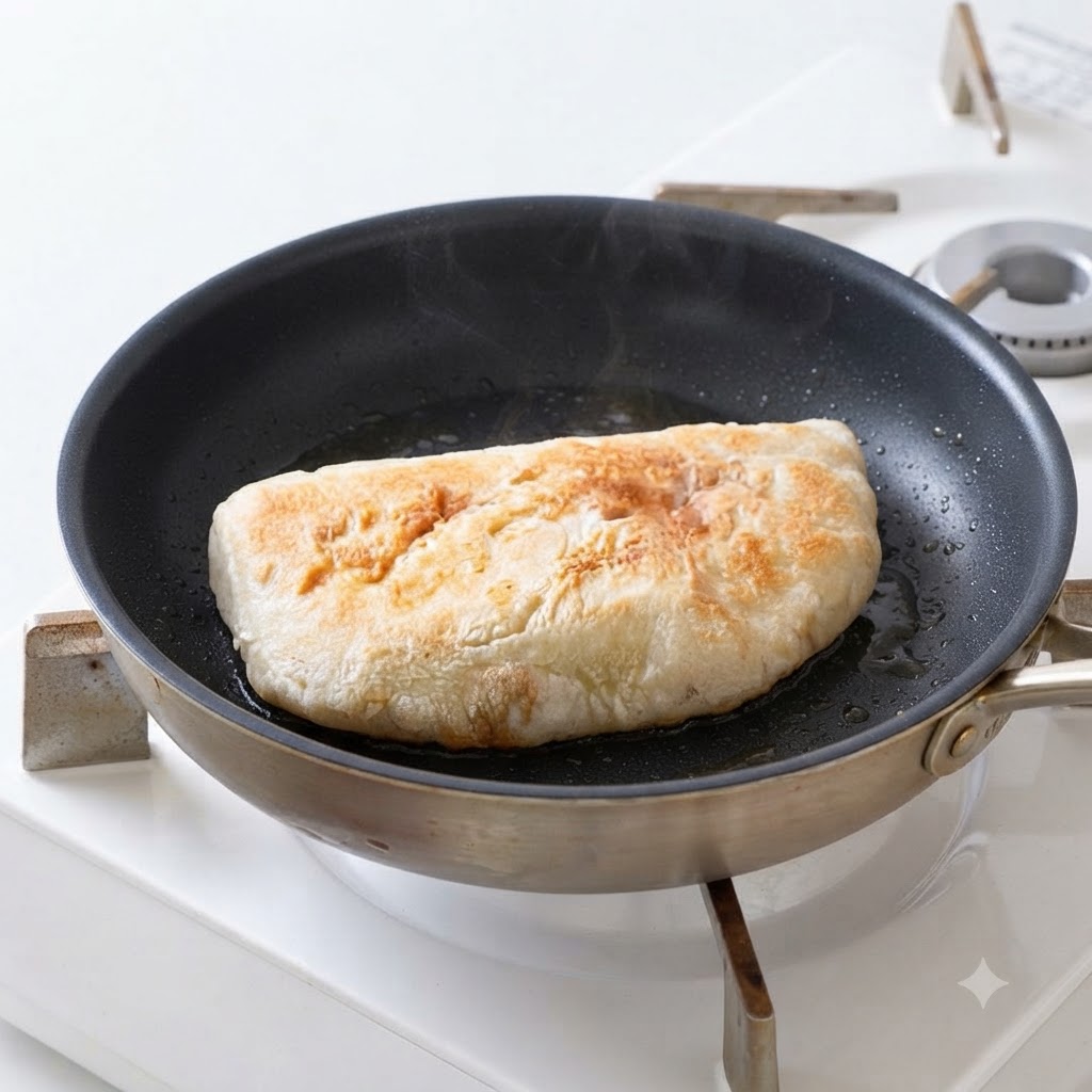 Metà di pane ciabatta che friggono nellolio dentro una padella fino a doratura e croccantezza.