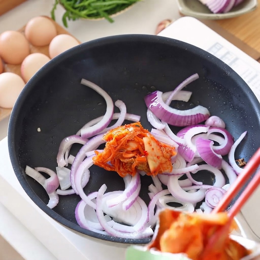 Kimchi fresco aggiunto con le bacchette in una padella contenente cipolle saltate.