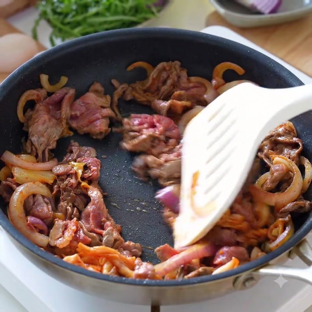 Manzo a fette, cipolle e kimchi saltati insieme in una padella con una spatola.