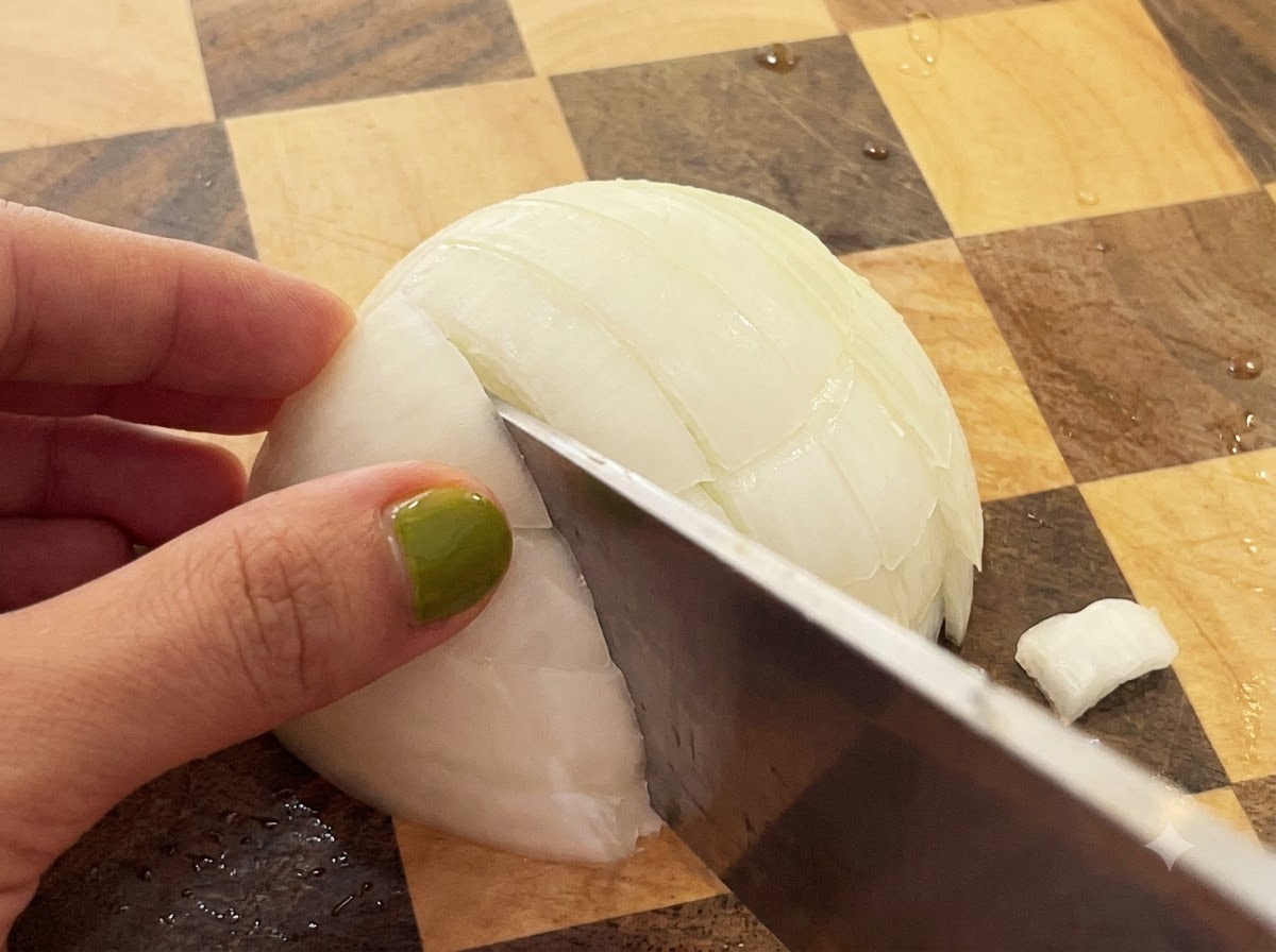Un coltello taglia a metà una cipolla bianca su un tagliere di legno a scacchi.
