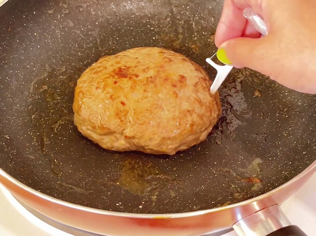 Uno stuzzicadenti che viene inserito sulla superficie superiore di un grosso hamburger cotto in una padella.
