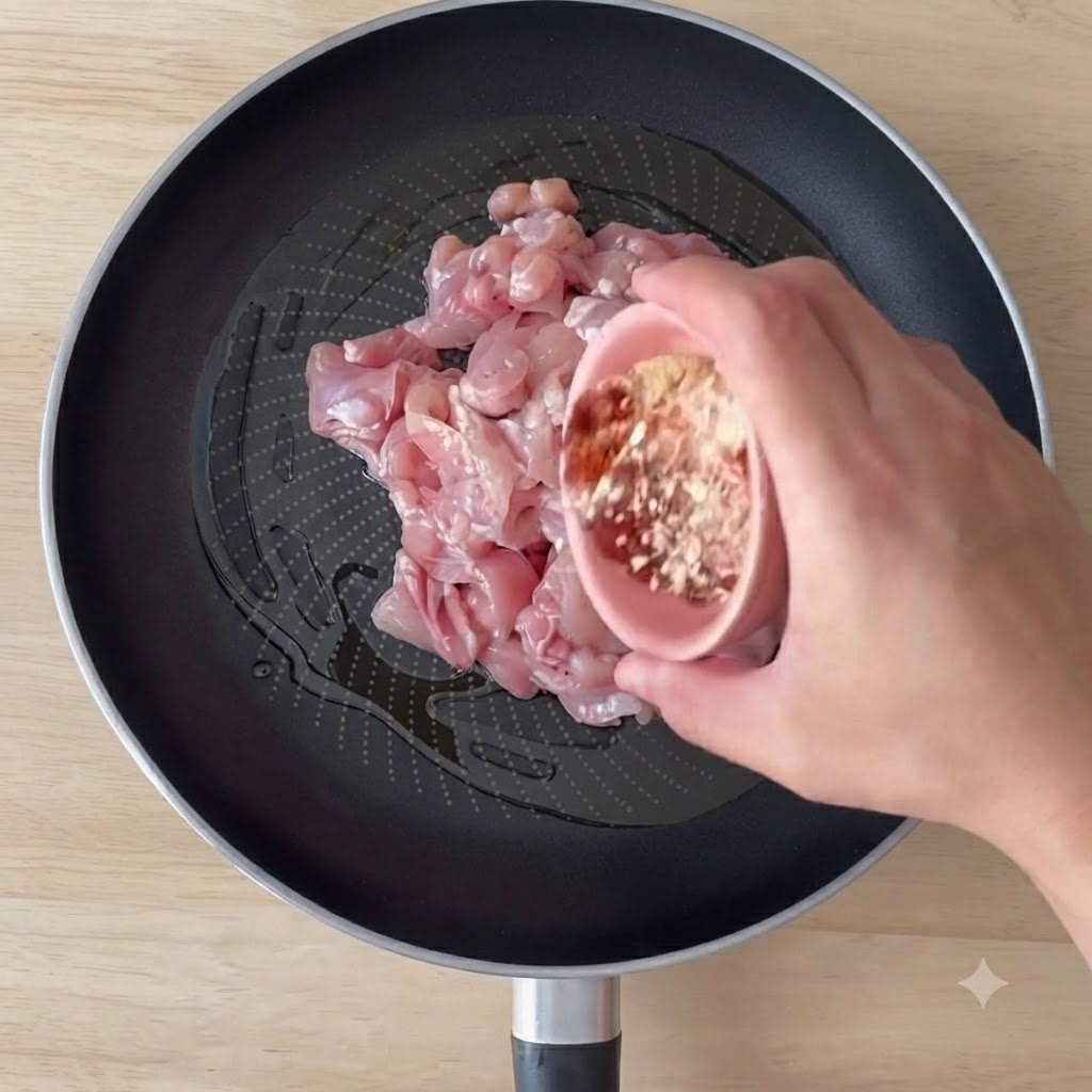 Pezzi di pollo disossato in cottura in padella con olio doliva e spezie, mentre vengono mescolati.