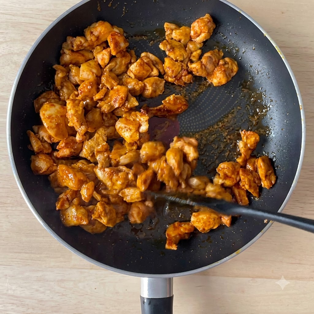 Salsa di soia versata in una padella con pezzetti di pollo rosolati.