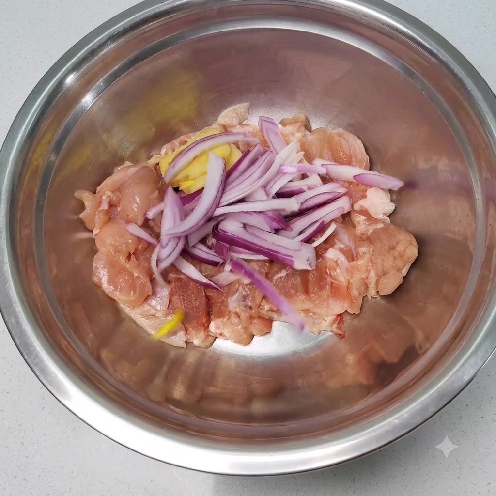 Pezzi di pollo crudo mescolati con cipolle affettate e zenzero allinterno di una ciotola di miscelazione in acciaio inossidabile.