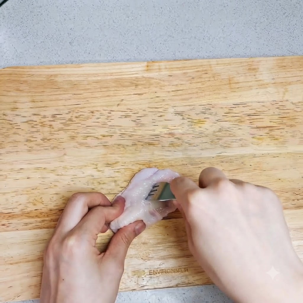 Un paio di mani che usano una forchetta per praticare dei fori su unala di pollo cruda su un tagliere.