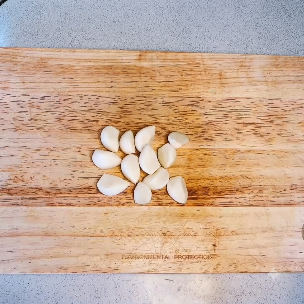 Spicchi daglio disposti su un tagliere di legno pronti per essere tritati.