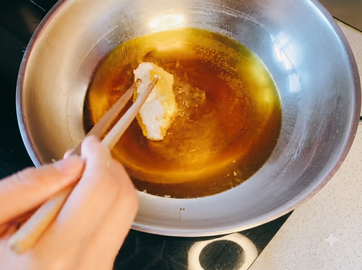 Bacchette che mettono un pezzo di pollo impanato in una padella di metallo piena di olio caldo.