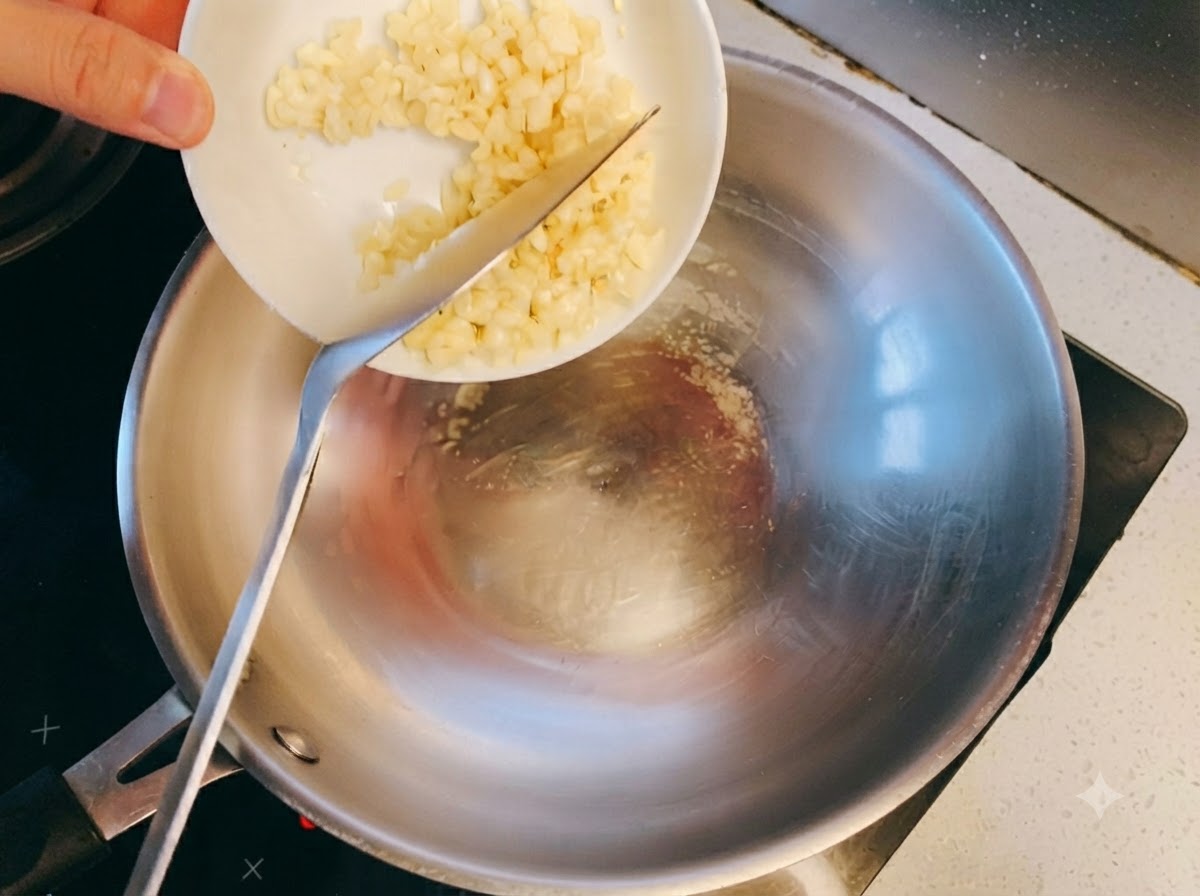 Aglio tritato che colpisce lolio caldo in un wok di acciaio inossidabile e inizia a dorare.