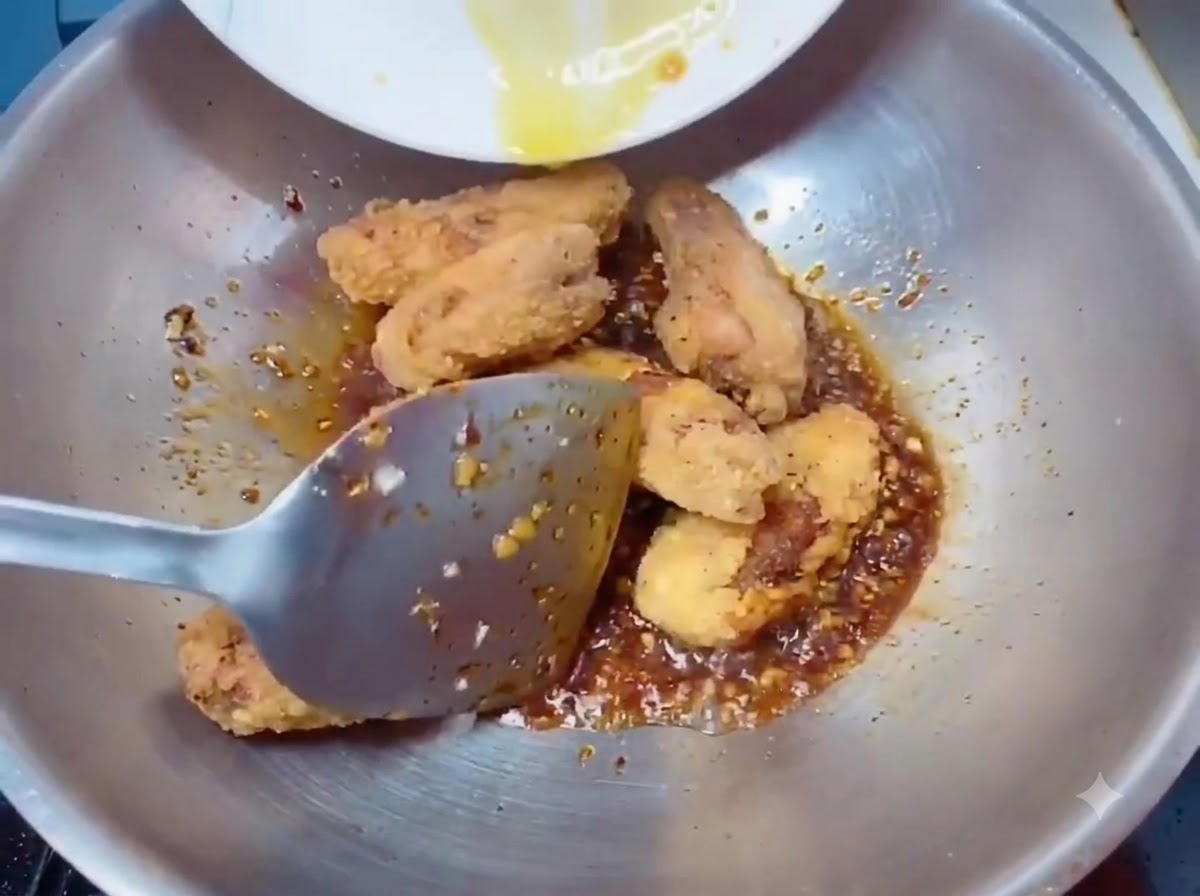Ali di pollo fritte croccanti e dorate trasferite nel wok con la salsa usando una spatola.