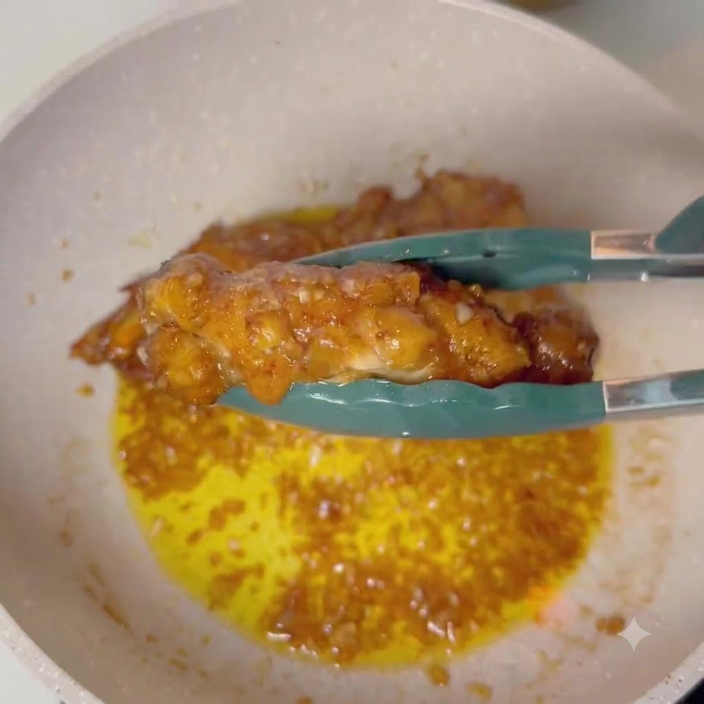 Pinze che tengono una coscia di pollo glassata sopra una padella con salsa al burro e aglio in ebollizione.