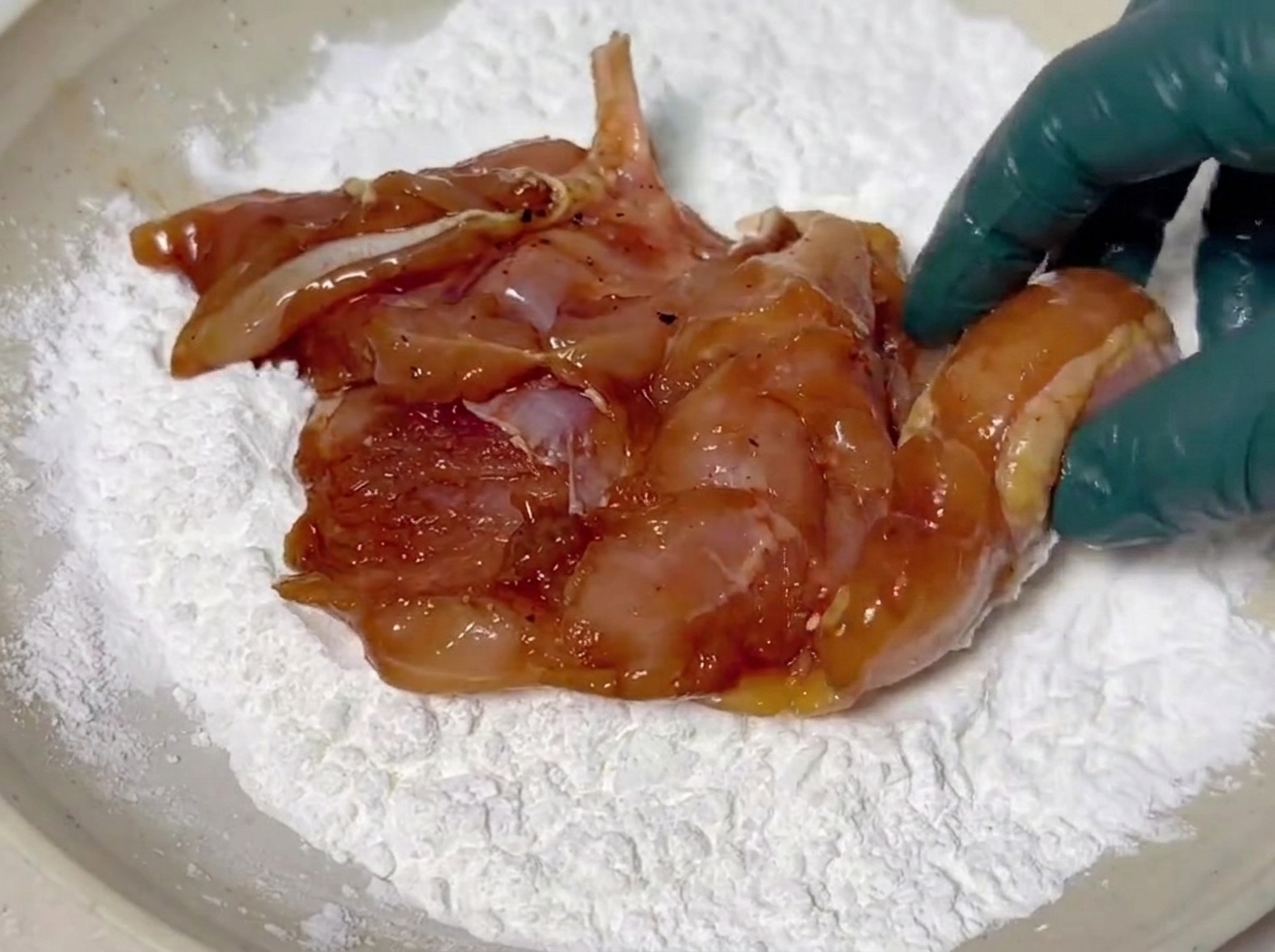 Pezzi di pollo marinati ricoperti da uno strato bianco di amido di mais in un piatto fondo.