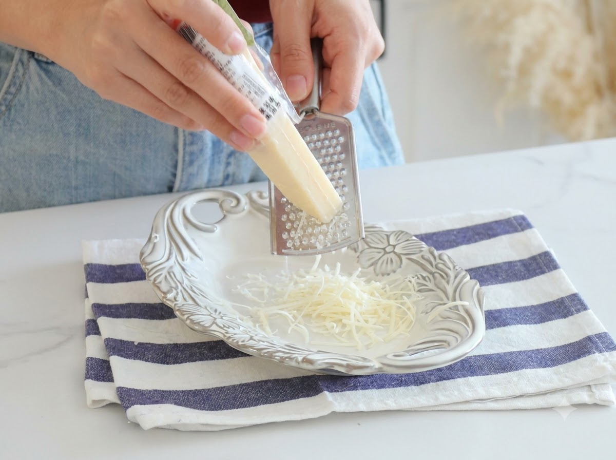 Parmigiano appena grattugiato con una grattugia di metallo su un piatto bianco.
